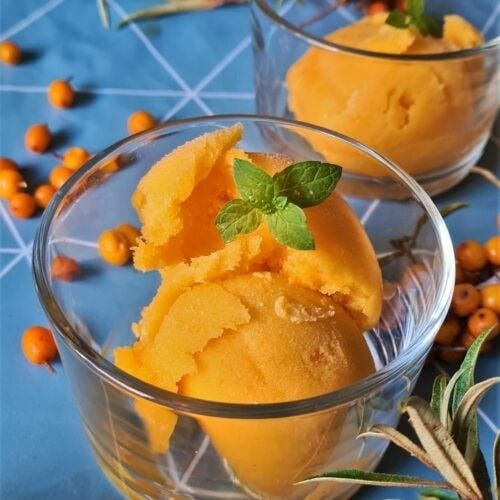 Orangefärgad sorbet i glasskålar, garnerad med mynta och havtorn